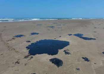 Manchas negras y viscosas de crudo esparcidas sobre la arena de una playa desierta, evidenciando un derrame-de-petróleo.