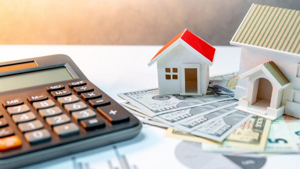 inversión-inmobiliaria-en-monterrey-quantium-desarrollos - VOZ Y OPINION Calculator and toy house models atop scattered dollar bills, indicating real estate investment or mortgage costs.