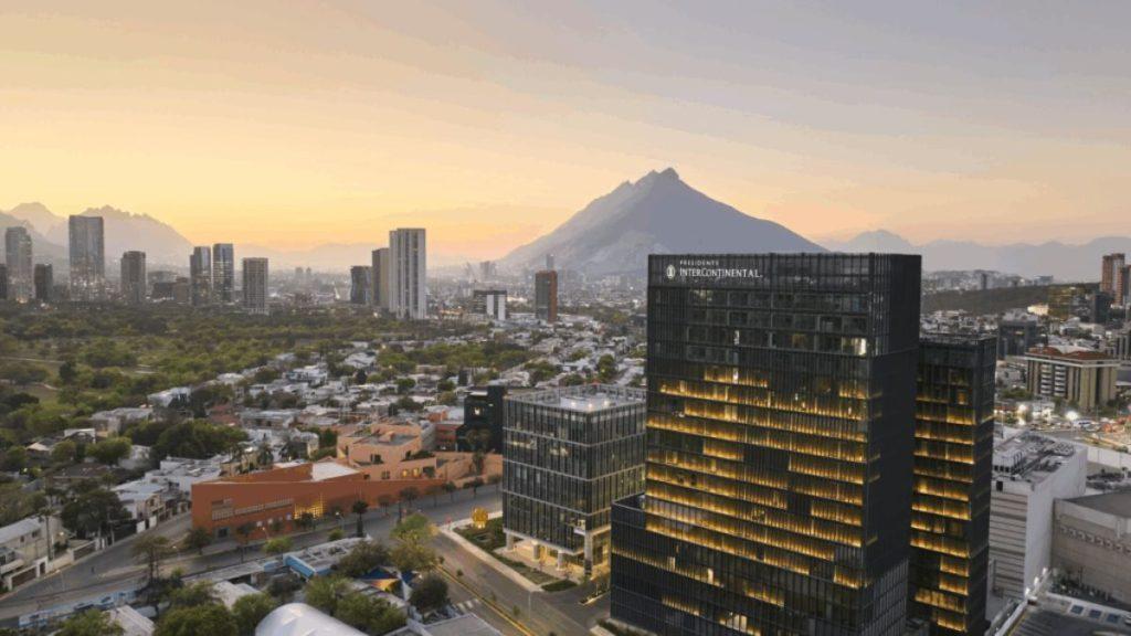 Aerial view of a modern city at sunset with glass office towers and a distant mountain range on the horizon.