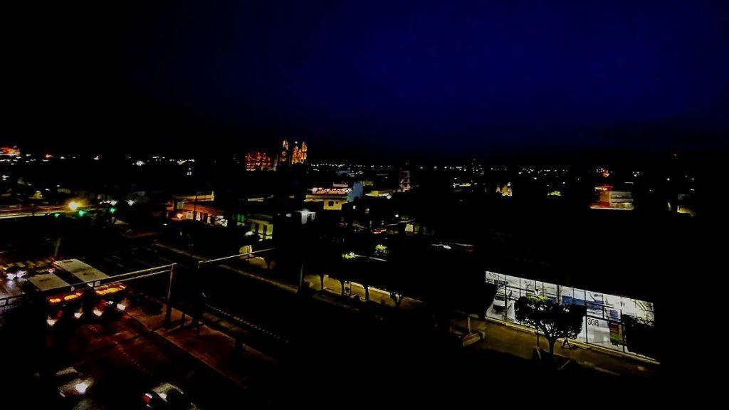 Night city skyline at dusk with scattered streetlights and illuminated buildings along a quiet street corridor.