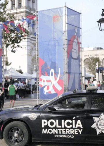la-logistica-de-resguardo-para-selecciones - VOZ Y OPINION Police car labeled Policía Monterrey in the foreground at an outdoor street festival with blue banners, tents, and people in the background.
