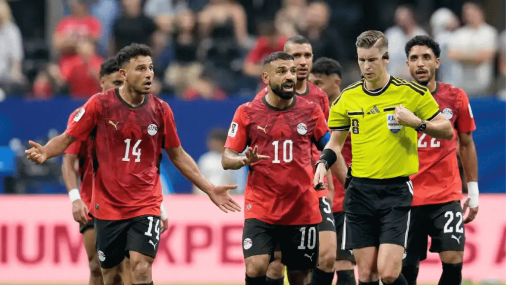 Egyptian national team players in red jerseys on the field with a referee in a bright yellow kit during a match.
