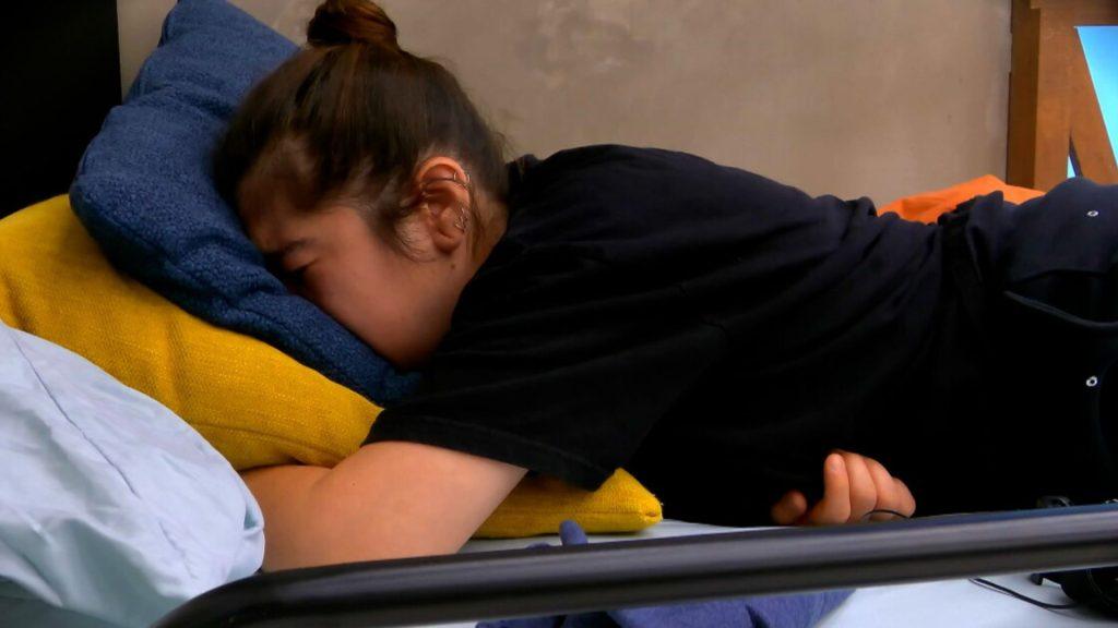 declaraciones-carmen-masterchef - VOZ Y OPINION Person lying on their side on a bed, head resting on a blue pillow with a yellow cushion beneath, wearing a black shirt.